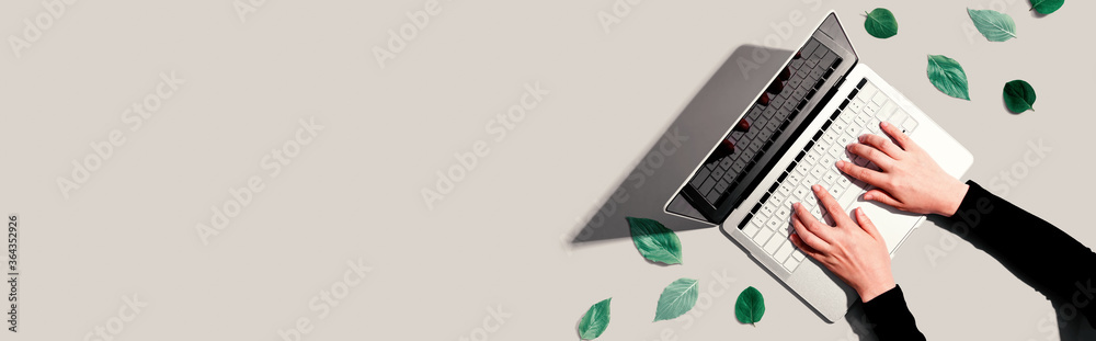 Person using a laptop computer with green leaves from above - obrazy, fototapety, plakaty 