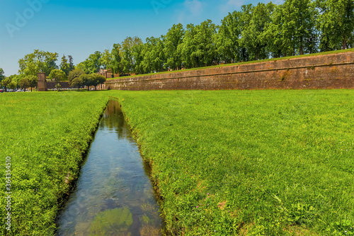 A view along a water channel towards the city walls of Lucca Italy in summer