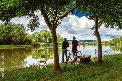 Two fishermen with fishing rods and a bicycle on the lake