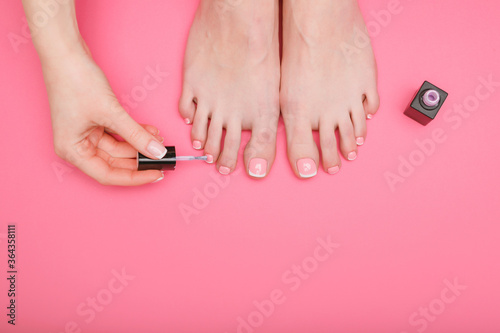 Closeup young well-groomed female foots. Woman doing pedicure and files nails. Girl applies nail polish. Pink background. Top view. Free space for text.