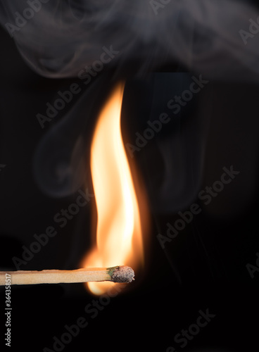 Match bursting into flame with smoke against black background.