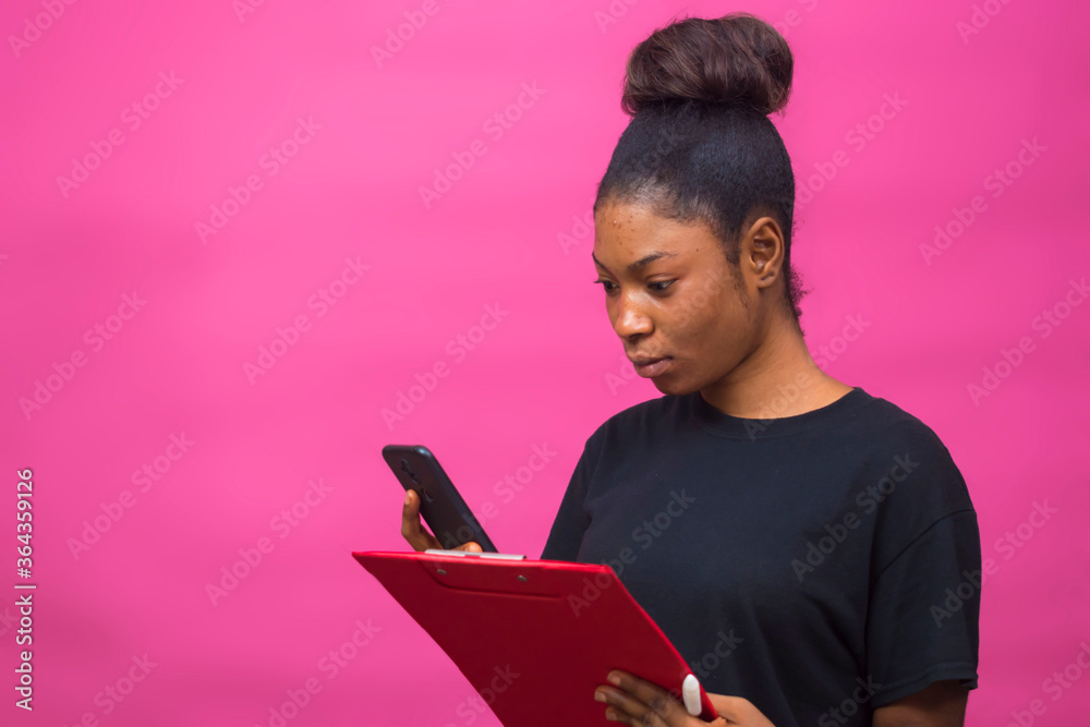 young beautiful black lady holding her notepad and using her smartphone check out something young beautiful black lady holding her notepad and using her smartphone check out something