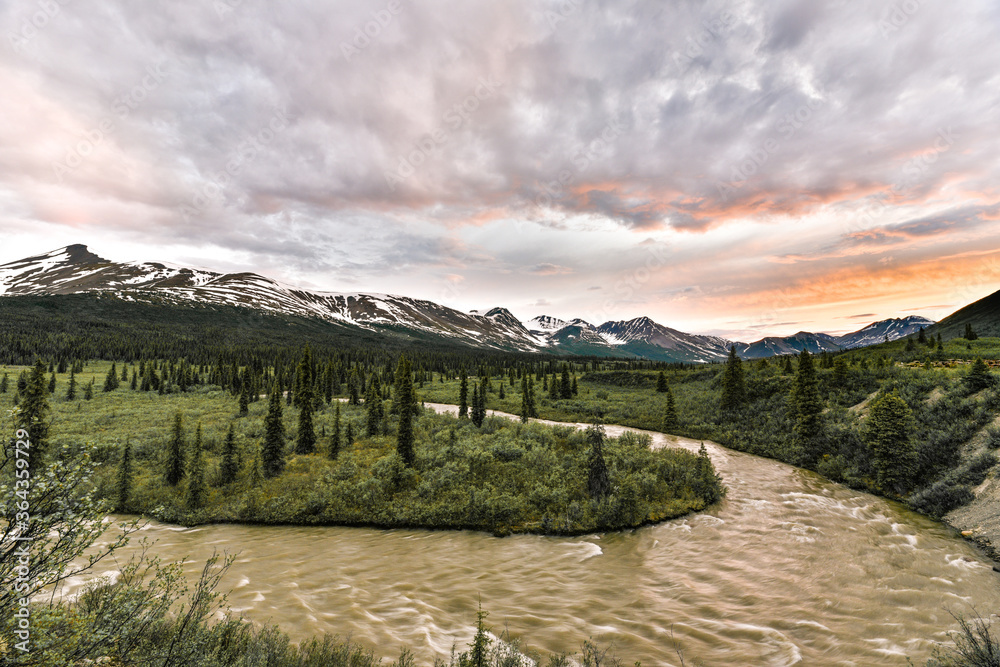 Stunning Canadian sunset with snow capped mountains & river in shot. Taken on the North Canol Road in Yukon Territory, northern Canada in the summer time. 