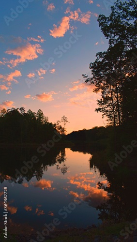 Sunset reflected in lake surrounded by forest with dark pink clouds © JMP Traveler