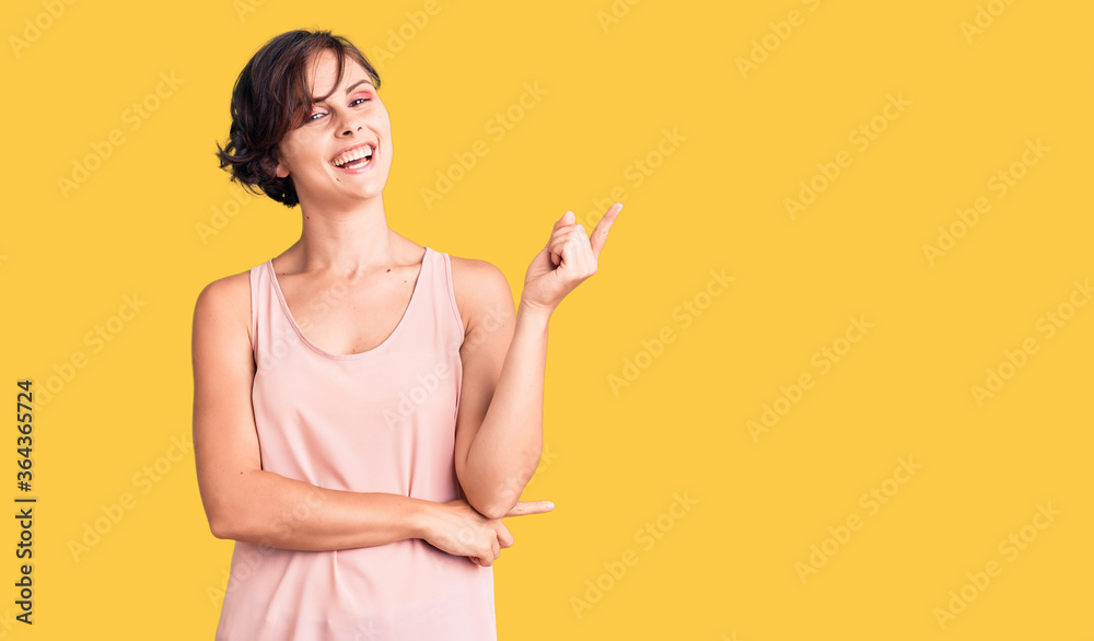 Beautiful young woman with short hair wearing casual style with sleeveless shirt with a big smile on face, pointing with hand and finger to the side looking at the camera. Beautiful young woman with short hair wearing casual style with sleeveless shirt with a big smile on face, pointing with hand and finger to the side looking at the camera.