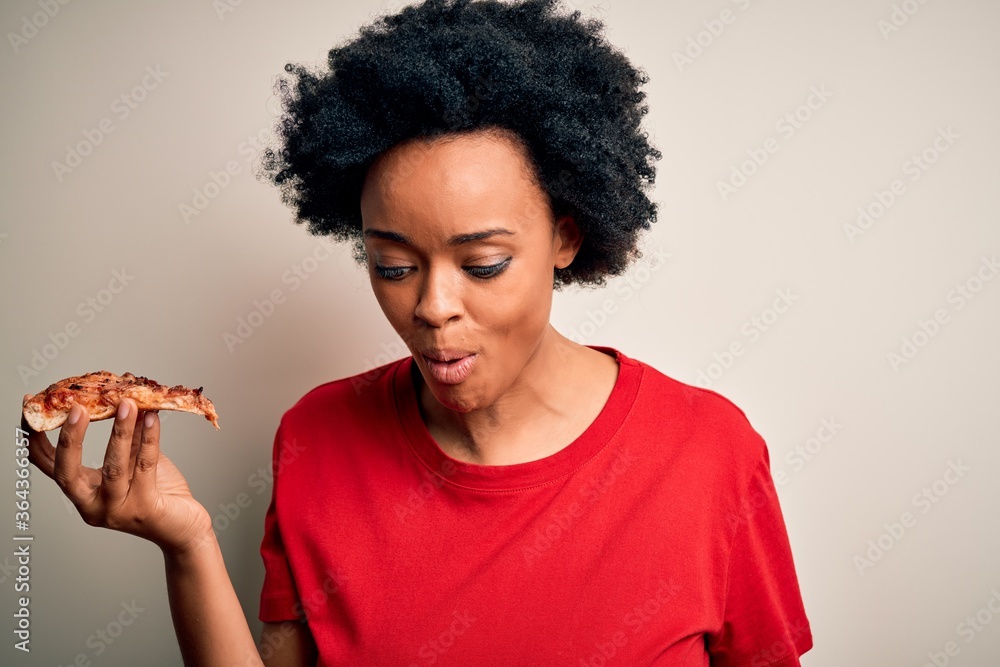 Young beautiful african american afro woman smiling happy and confident. Standing with smile on face eating delicious slice of italian pizza over isolated white background Young beautiful african american afro woman smiling happy and confident. Standing with smile on face eating delicious slice of italian pizza over isolated white background