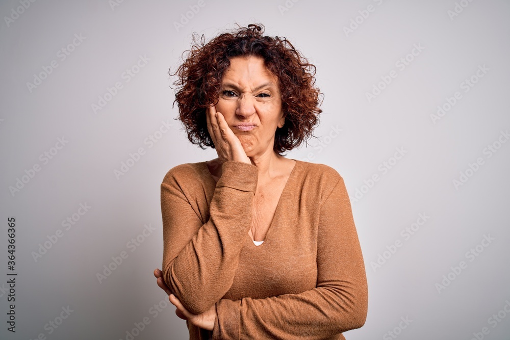 Middle age beautiful curly hair woman wearing casual sweater over isolated white background thinking looking tired and bored with depression problems with crossed arms. Middle age beautiful curly hair woman wearing casual sweater over isolated white background thinking looking tired and bored with depression problems with crossed arms.