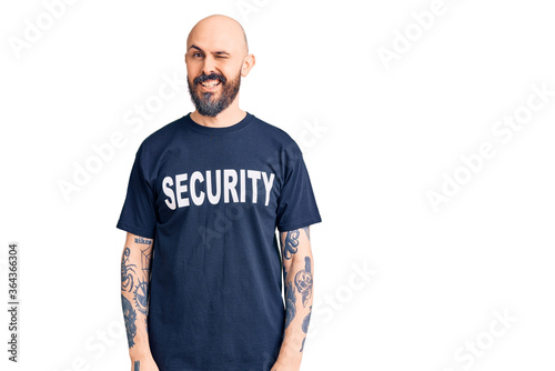 Young handsome man wearing security t shirt winking looking at the camera with sexy expression, cheerful and happy face.