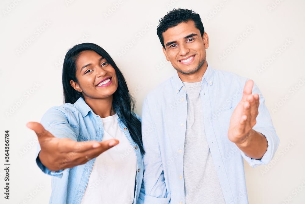 Beautiful latin young couple wearing casual clothes smiling friendly offering handshake as greeting and welcoming. successful business. Beautiful latin young couple wearing casual clothes smiling friendly offering handshake as greeting and welcoming. successful business.