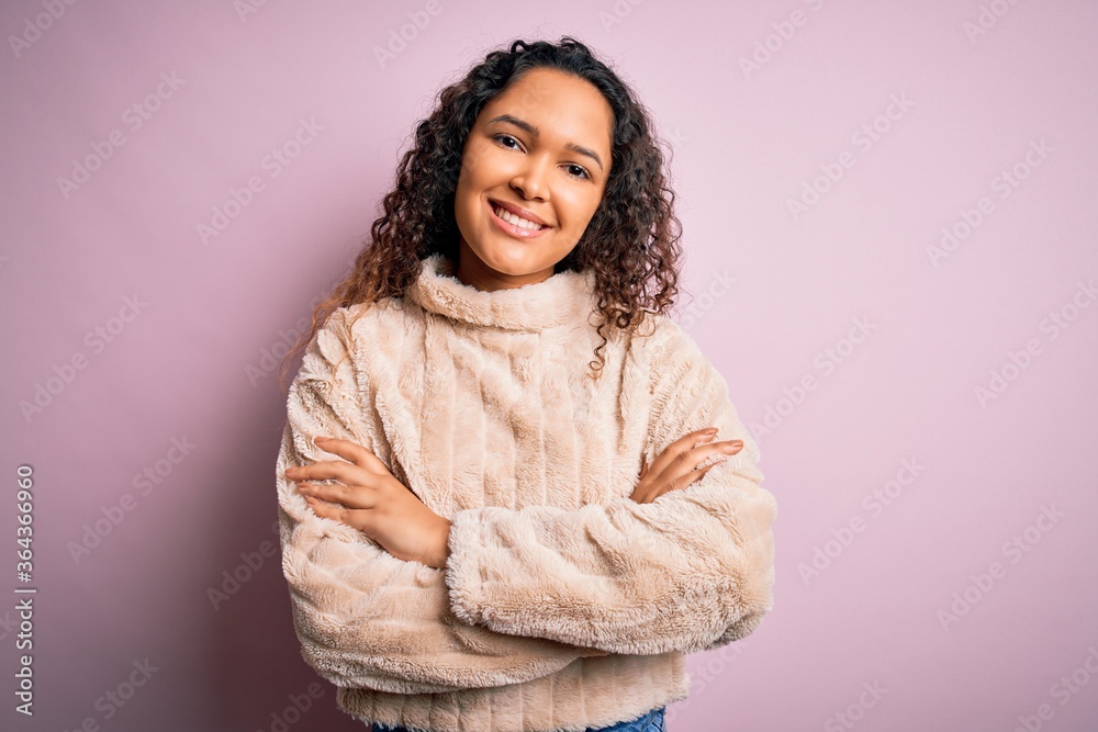 Young beautiful woman with curly hair wearing casual sweater standing over pink background happy face smiling with crossed arms looking at the camera. Positive person. Young beautiful woman with curly hair wearing casual sweater standing over pink background happy face smiling with crossed arms looking at the camera. Positive person.