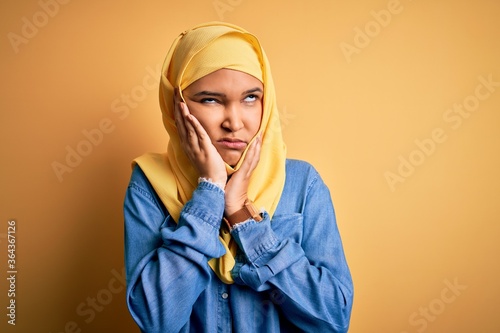 Young beautiful woman with curly hair wearing arab traditional hijab over yellow background Tired hands covering face, depression and sadness, upset and irritated for problem © Krakenimages.com