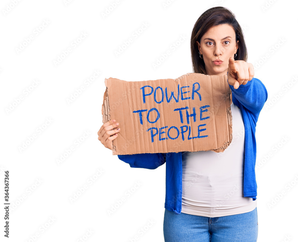 Young beautiful woman holding power to the people banner pointing with finger to the camera and to you, confident gesture looking serious Young beautiful woman holding power to the people banner pointing with finger to the camera and to you, confident gesture looking serious