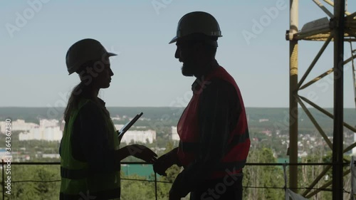 A Caucasian bearded worker in a protective helmet and orange vest shakes hands with a quality control engineer. Business handshake.