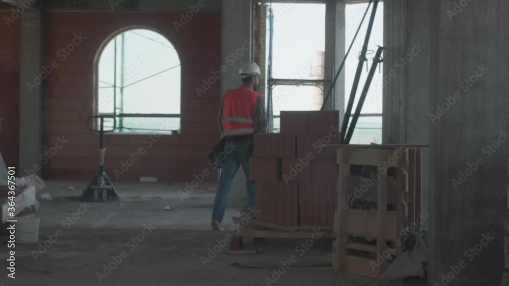 A worker with a beard wearing a protective orange vest and a hard hat while working on a construction site A worker with a beard wearing a protective orange vest and a hard hat while working on a construction site