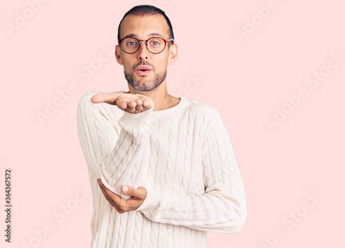 Young handsome man wearing casual clothes and glasses looking at the camera blowing a kiss with hand on air being lovely and sexy. love expression.