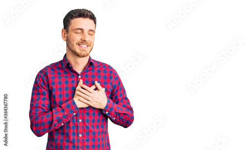 Handsome young man with bear wearing casual shirt smiling with hands on chest with closed eyes and grateful gesture on face. health concept.