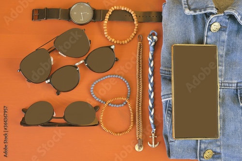 Top view of men accessories. Hipster or modern man concept. Accessories for going for a walk. Male fashion accessories, flat lay on coral pink background. Bracelets, sunglasses - shades, watch -