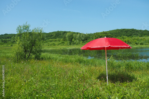 Red sunshade on green grass in the background of a small lake.