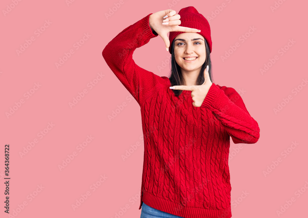 Fototapeta premium Young beautiful girl wearing sweater and wool cap smiling making frame with hands and fingers with happy face. creativity and photography concept.