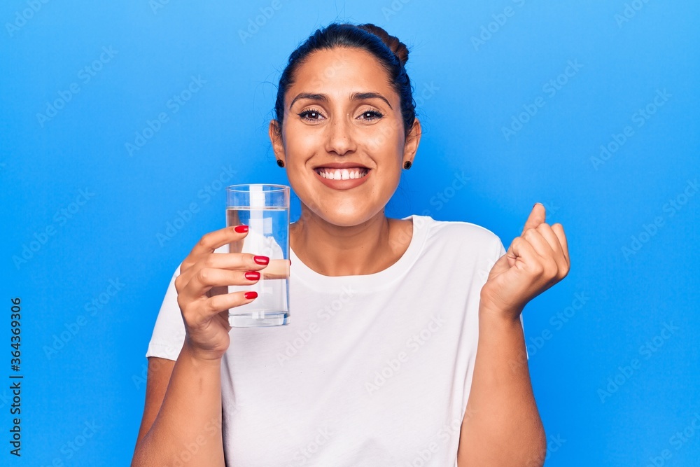 Young beautiful brunette woman drinking glass of water screaming proud, celebrating victory and success very excited with raised arm Young beautiful brunette woman drinking glass of water screaming proud, celebrating victory and success very excited with raised arm