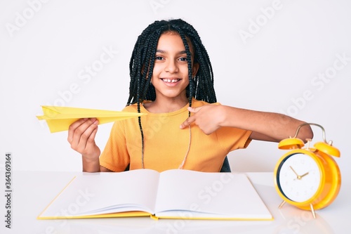 Young african american girl child with braids holding paper airplane while studying pointing finger to one self smiling happy and proud photo