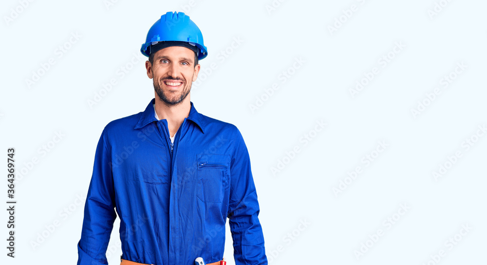 Young handsome man wearing worker uniform and hardhat with a happy and cool smile on face. lucky person. Young handsome man wearing worker uniform and hardhat with a happy and cool smile on face. lucky person.