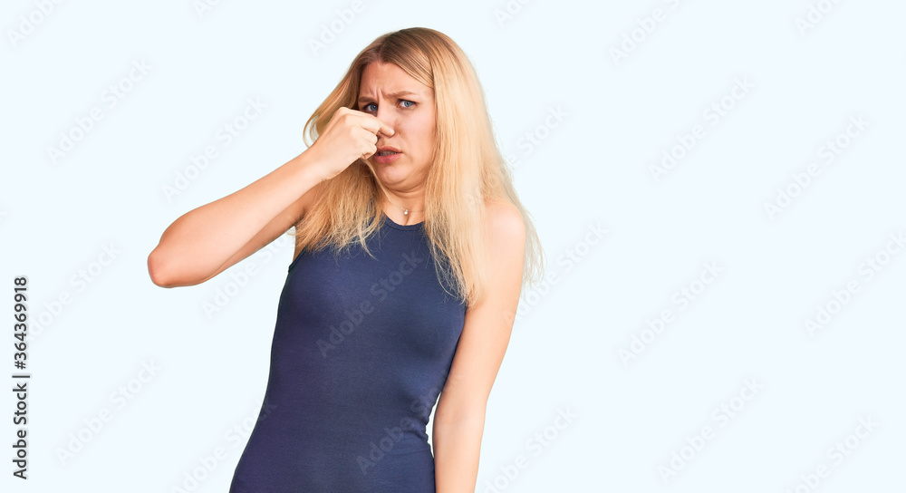 Young beautiful blonde woman wearing casual dress smelling something stinky and disgusting, intolerable smell, holding breath with fingers on nose. bad smell Young beautiful blonde woman wearing casual dress smelling something stinky and disgusting, intolerable smell, holding breath with fingers on nose. bad smell