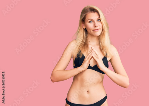 Young beautiful blonde woman wearing bikini hands together and fingers crossed smiling relaxed and cheerful. success and optimistic © Krakenimages.com