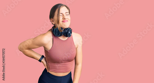 Beautiful caucasian young woman wearing gym clothes and using headphones suffering of backache, touching back with hand, muscular pain © Krakenimages.com