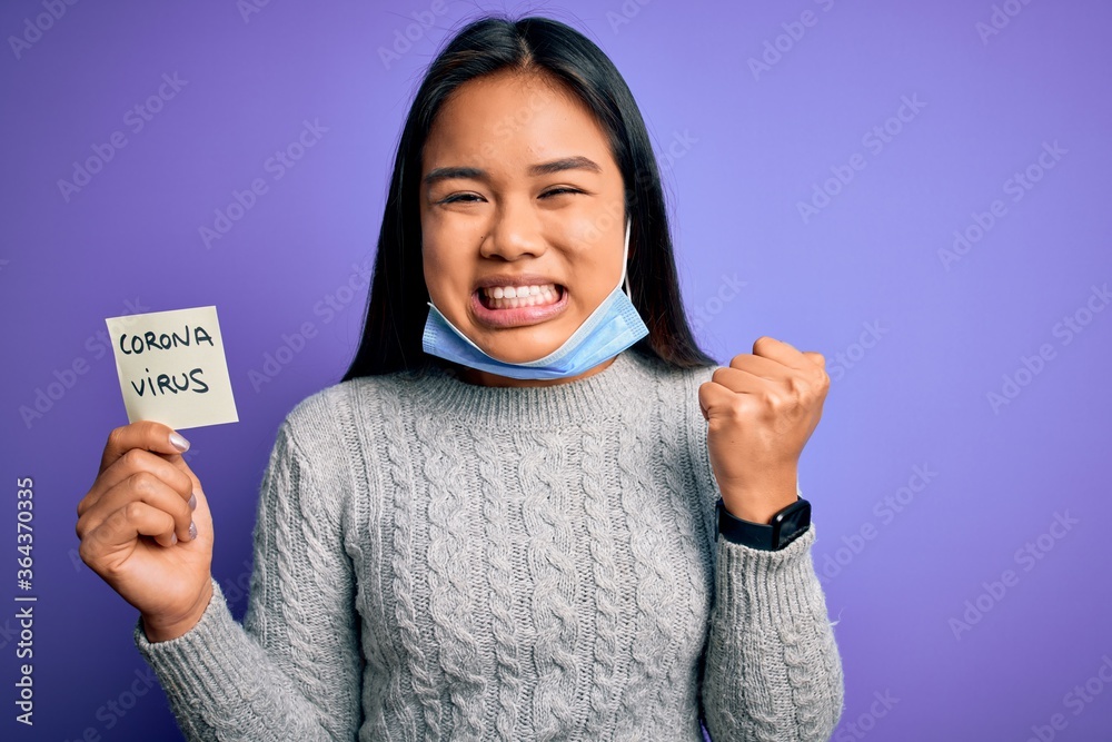 Asian girl wearing medical mask asking for alert holding reminder with corona virus message screaming proud and celebrating victory and success very excited, cheering emotion