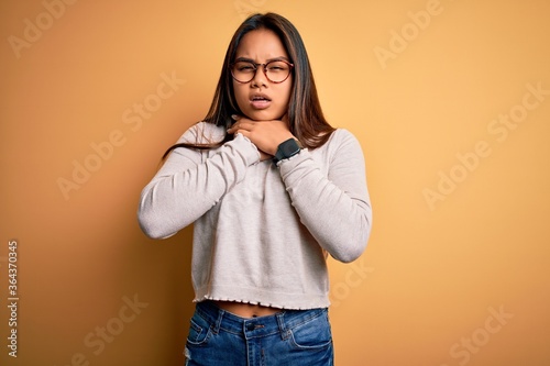 Young beautiful asian girl wearing casual sweater and glasses over yellow background shouting and suffocate because painful strangle. Health problem. Asphyxiate and suicide concept.