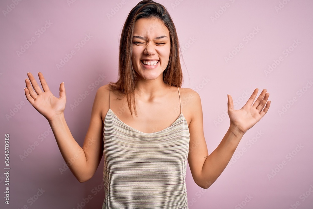 Young beautiful brunette girl wearing casual striped t-shirt over isolated pink background celebrating mad and crazy for success with arms raised and closed eyes screaming excited. Winner concept Young beautiful brunette girl wearing casual striped t-shirt over isolated pink background celebrating mad and crazy for success with arms raised and closed eyes screaming excited. Winner concept