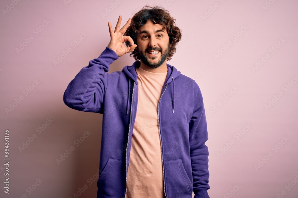 Young handsome sporty man with beard wearing casual sweatshirt over pink background smiling positive doing ok sign with hand and fingers. Successful expression. Young handsome sporty man with beard wearing casual sweatshirt over pink background smiling positive doing ok sign with hand and fingers. Successful expression.