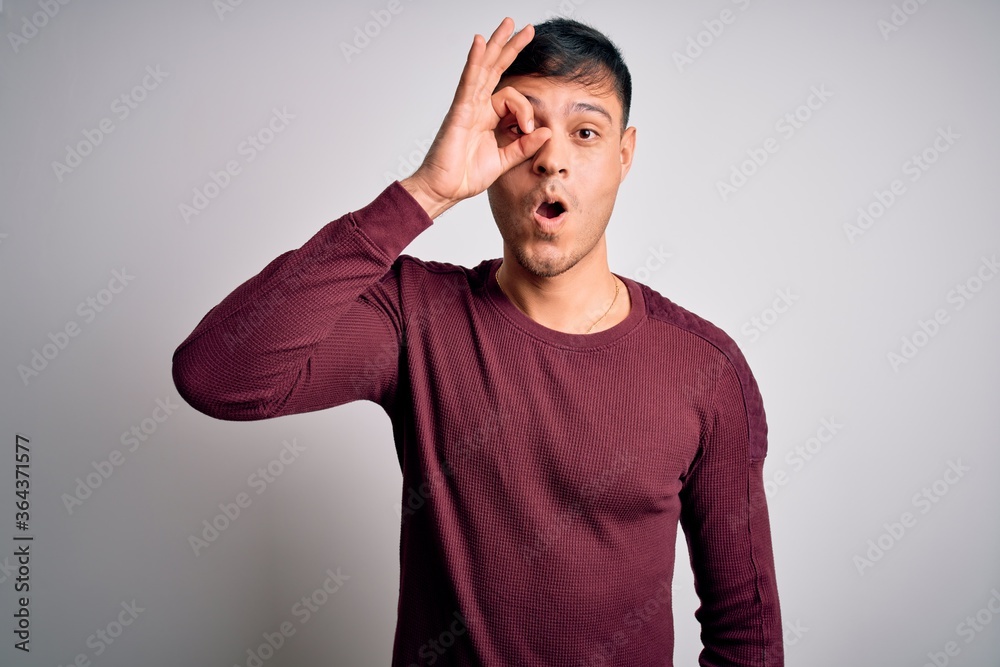 Young handsome hispanic man wearing casual shirt standing over white isolated background doing ok gesture shocked with surprised face, eye looking through fingers. Unbelieving expression. Young handsome hispanic man wearing casual shirt standing over white isolated background doing ok gesture shocked with surprised face, eye looking through fingers. Unbelieving expression.