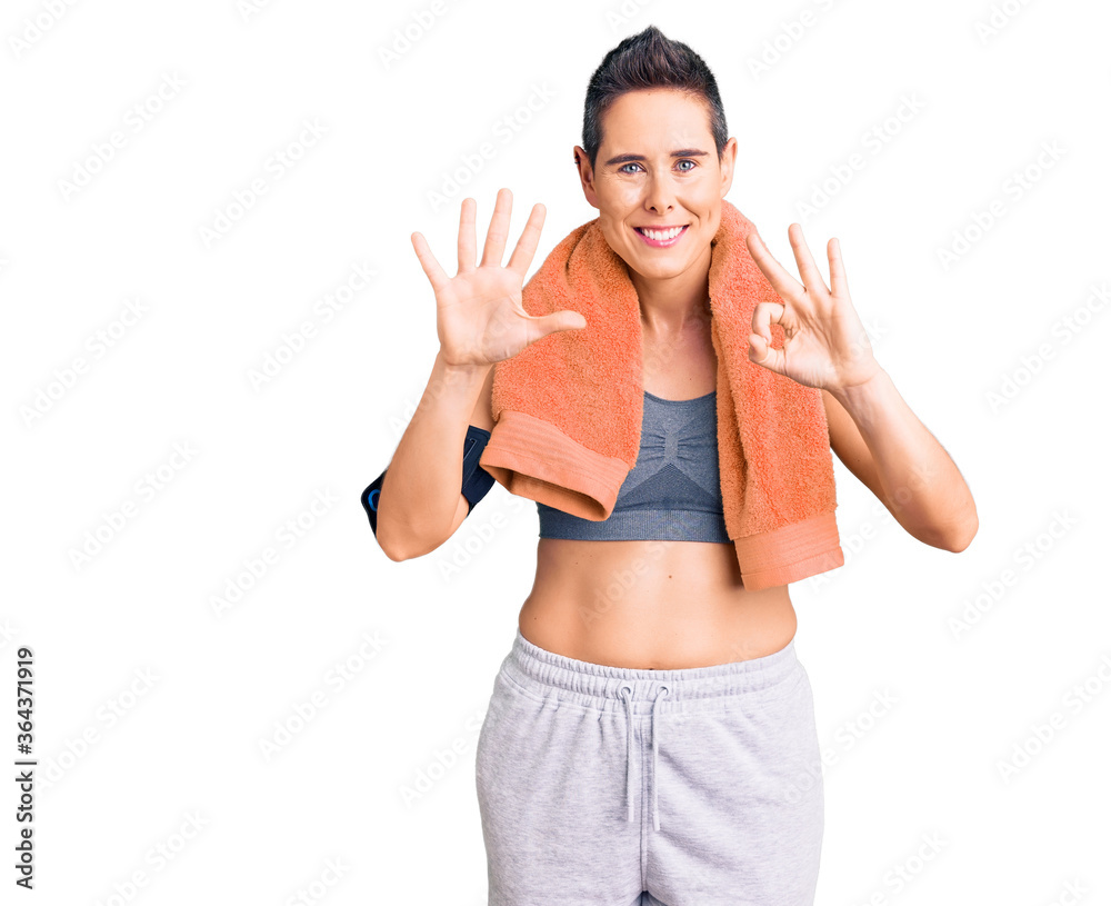 Young woman with short hair wearing sportswear and towel using smartphone showing and pointing up with fingers number eight while smiling confident and happy. Young woman with short hair wearing sportswear and towel using smartphone showing and pointing up with fingers number eight while smiling confident and happy.