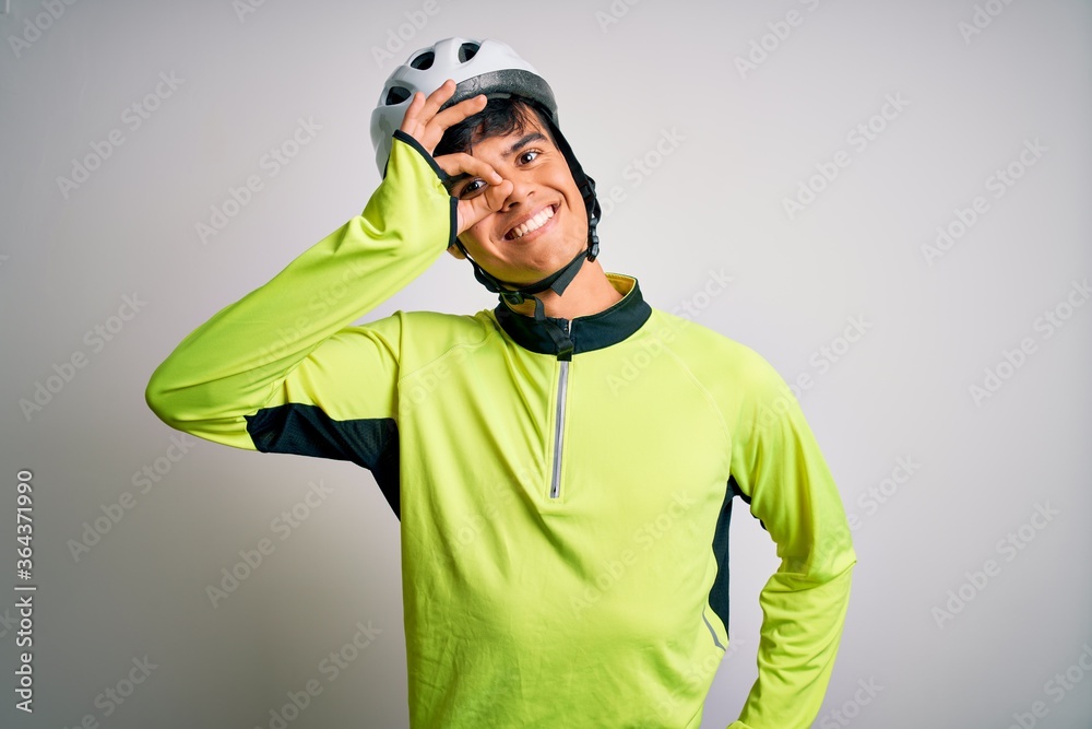 Young handsome cyclist man wearing security bike helmet over isolated white background doing ok gesture with hand smiling, eye looking through fingers with happy face. Young handsome cyclist man wearing security bike helmet over isolated white background doing ok gesture with hand smiling, eye looking through fingers with happy face.