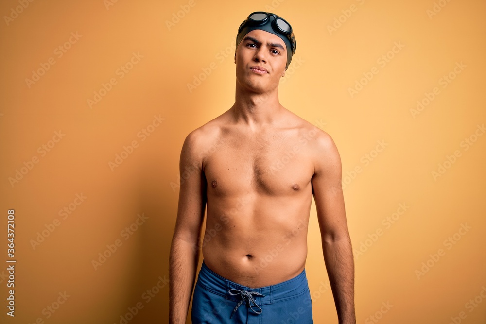 Young handsome man shirtless wearing swimsuit and swim cap over isolated yellow background looking sleepy and tired, exhausted for fatigue and hangover, lazy eyes in the morning.