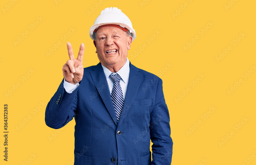 Senior handsome grey-haired man wearing suit and architect hardhat smiling with happy face winking at the camera doing victory sign. number two. Senior handsome grey-haired man wearing suit and architect hardhat smiling with happy face winking at the camera doing victory sign. number two.