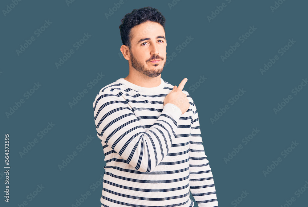Young hispanic man wearing casual clothes pointing with hand finger to the side showing advertisement, serious and calm face Young hispanic man wearing casual clothes pointing with hand finger to the side showing advertisement, serious and calm face