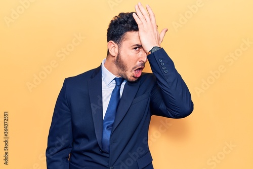 Young hispanic man wearing suit surprised with hand on head for mistake, remember error. forgot, bad memory concept.