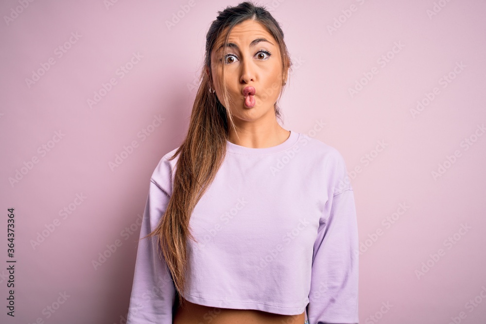 Young beautiful sport woman wearing sweatshirt over pink isolated background making fish face with lips, crazy and comical gesture. Funny expression. Young beautiful sport woman wearing sweatshirt over pink isolated background making fish face with lips, crazy and comical gesture. Funny expression.