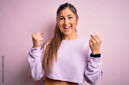 Young beautiful sport woman wearing sweatshirt over pink isolated background celebrating surprised and amazed for success with arms raised and open eyes. Winner concept.