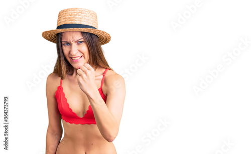 Beautiful brunette young woman wearing bikini angry and mad raising fist frustrated and furious while shouting with anger. rage and aggressive concept.