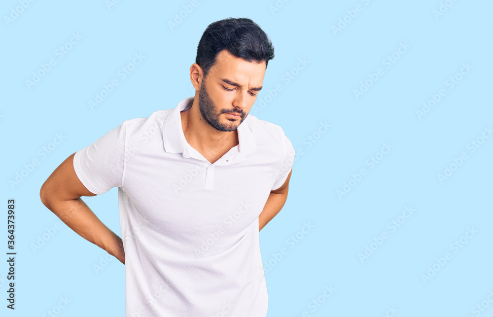 Young handsome hispanic man wearing casual clothes suffering of backache, touching back with hand, muscular pain Young handsome hispanic man wearing casual clothes suffering of backache, touching back with hand, muscular pain