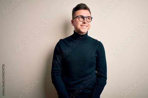 Young handsome caucasian man wearing glasses and casual sweater over isolated background looking away to side with smile on face, natural expression. Laughing confident.