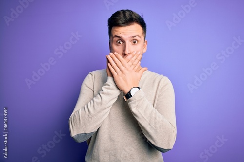 Young handsome caucasian man wearing casual sweater over purple isolated background shocked covering mouth with hands for mistake. Secret concept.