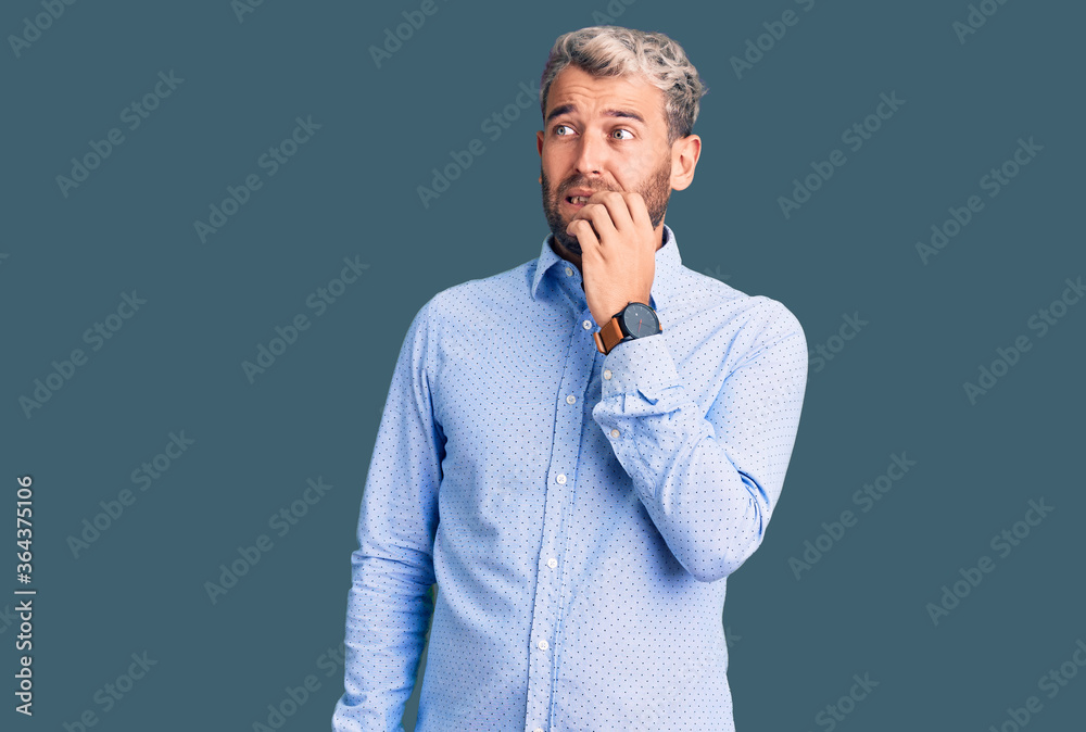 Young handsome blond man wearing elegant shirt looking stressed and nervous with hands on mouth biting nails. anxiety problem. Young handsome blond man wearing elegant shirt looking stressed and nervous with hands on mouth biting nails. anxiety problem.