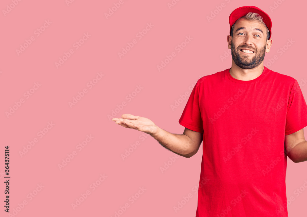 Naklejka premium Young handsome blond man wearing t-shirt and cap clueless and confused expression with arms and hands raised. doubt concept.
