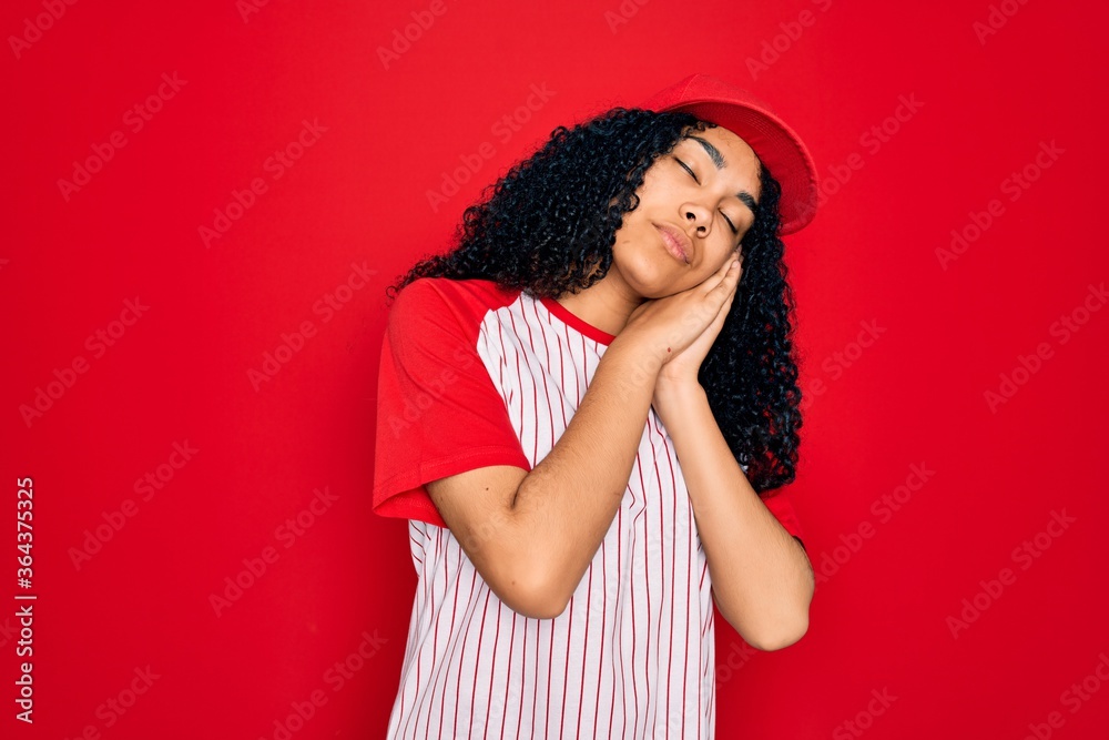 Young african american curly sportswoman wearing baseball cap and striped t-shirt sleeping tired dreaming and posing with hands together while smiling with closed eyes. Young african american curly sportswoman wearing baseball cap and striped t-shirt sleeping tired dreaming and posing with hands together while smiling with closed eyes.