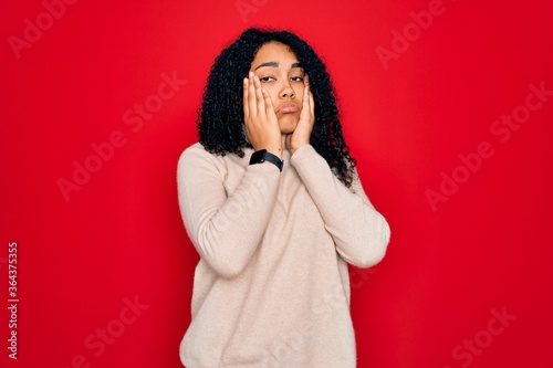 Young african american curly woman wearing casual turtleneck sweater over red background Tired hands covering face, depression and sadness, upset and irritated for problem © Krakenimages.com